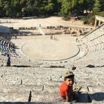 bambino seduto con cappellino siullo sfondo teatro greco antico