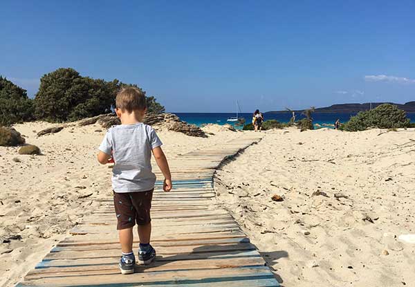 bambino di spalle su passerella di legno che porta al male