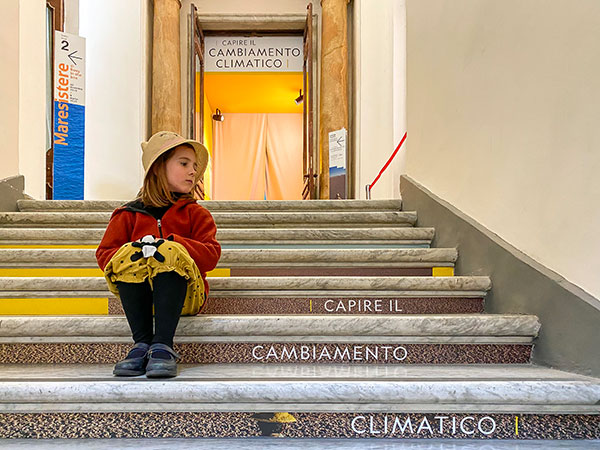 mostra cambiamento climatico bambina seduta sui gradini con la scritta