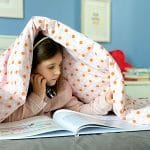 bambina legge libro sotto le coperte