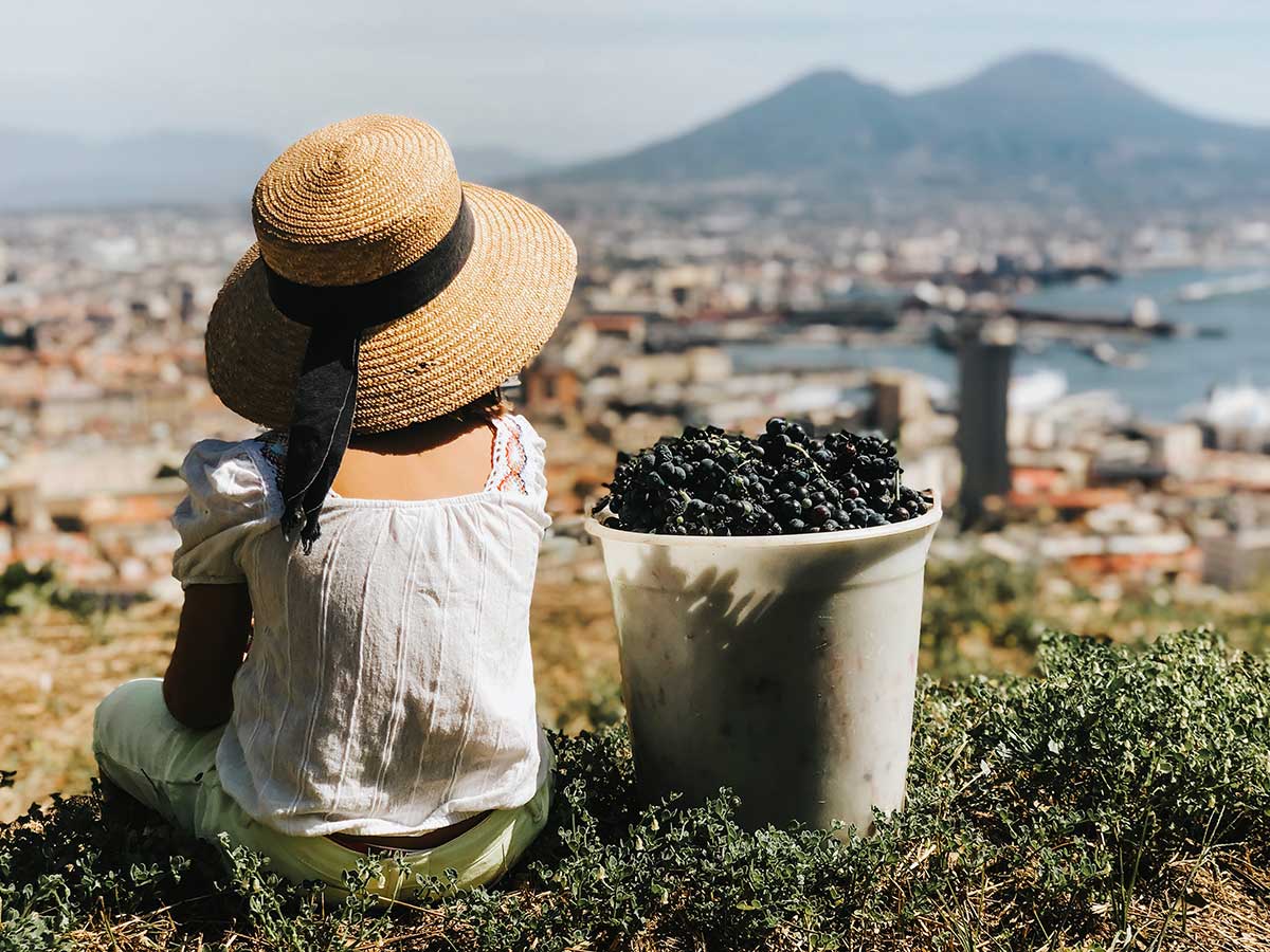 bambina di spalle con secchio uva e vesuvio sullo sfondo