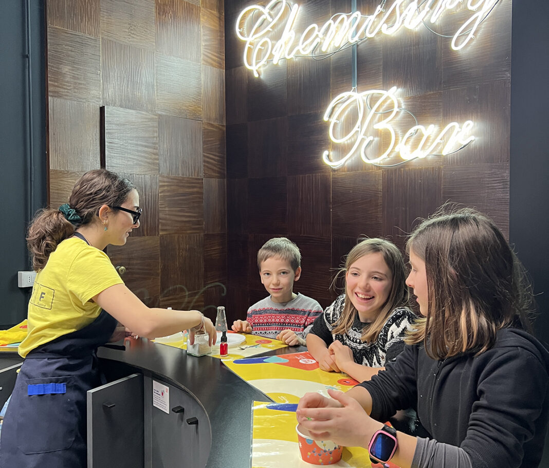 bar della chimica tre bambini fanno gli esperimenti con la barista