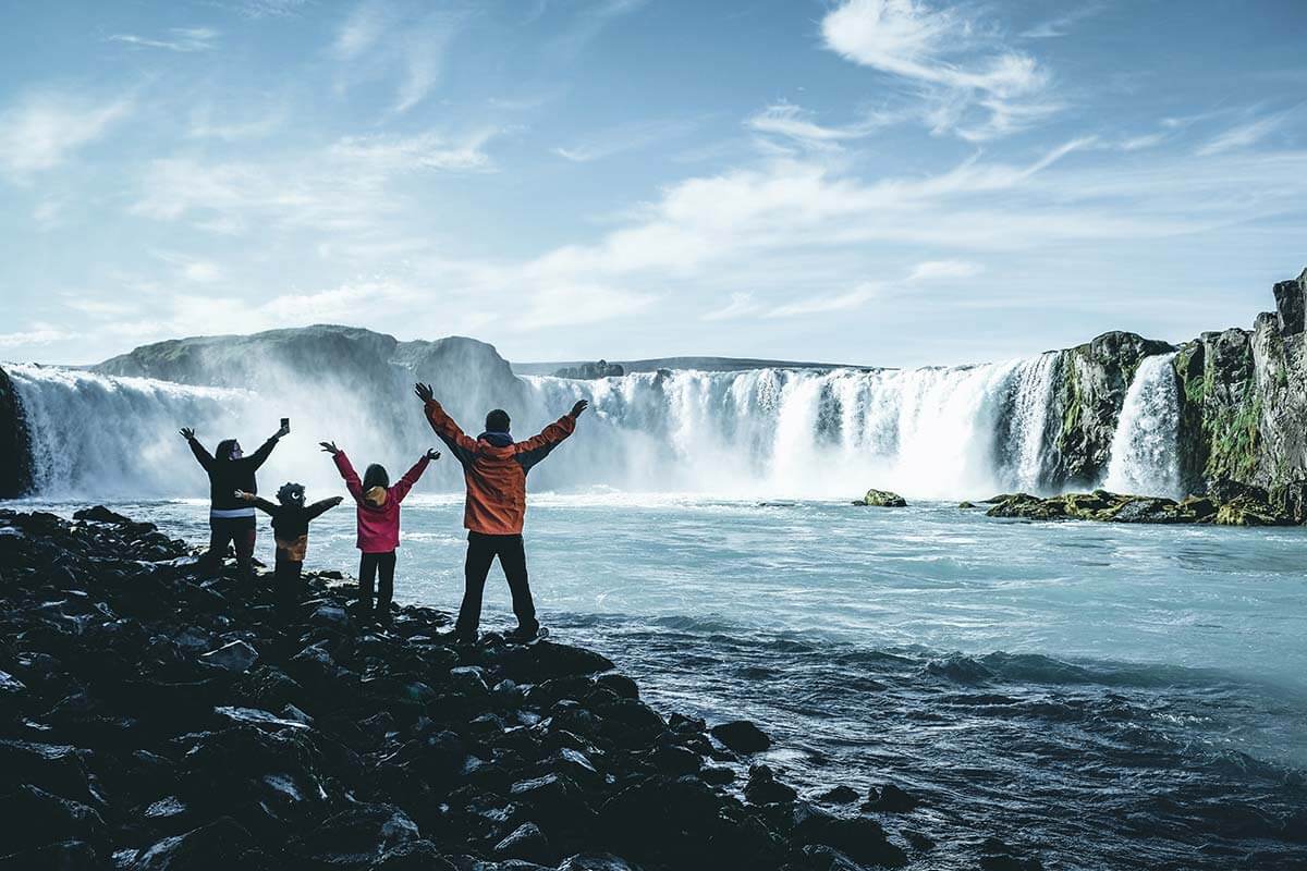 famiglia con le braccia aperte in alto davanti alla cascata di Godafoss in Islanda