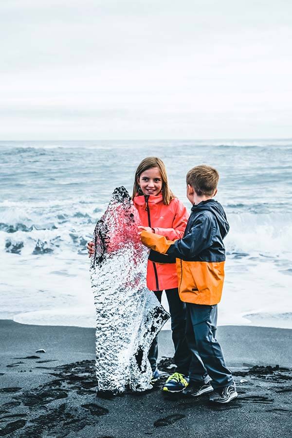 bambini giocano con una grande pezzo di ghiaccio sulla riva della spiaggia nera