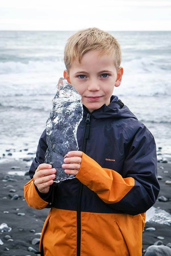 bambino con in mano un pezzo di ghiaccio sulla riga dell'oceano in Islanda