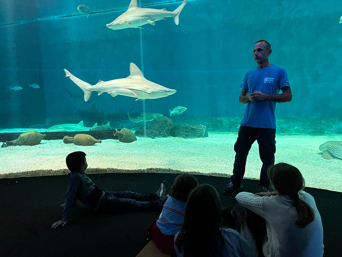 Membro dello staff dell'acquario con i bambini di fronte alla vasca degli squali