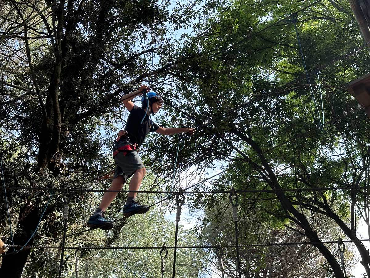parco avventura ragazzino sopseso su un filo tra gli alberti