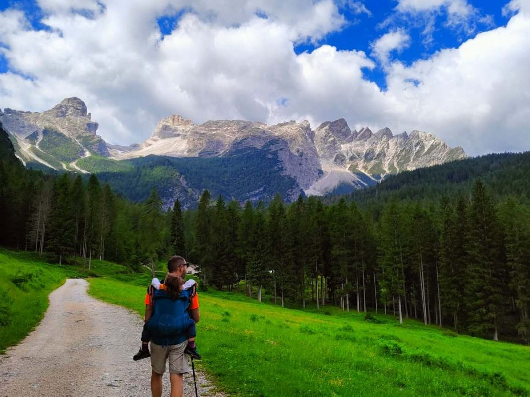 papà con bimba in marsupio davanti alle montagne