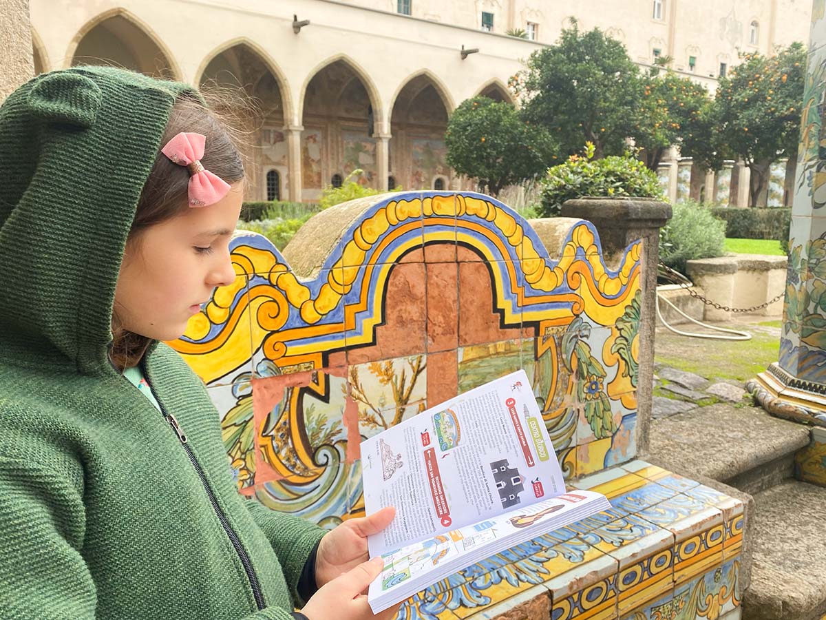 Bambina legge Guida di napoli per bambini nel chiostro di Santa Chiara